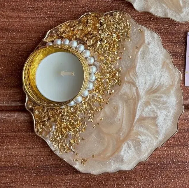 A pearl-cream resin tealight holder with a scalloped gilded edge, a drift of gold flake across one side and a ring of pearls around the brass cup