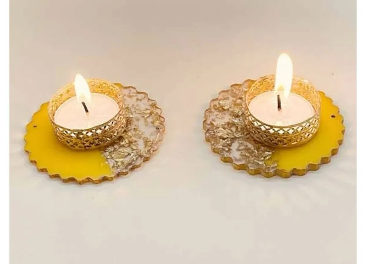 Two round marigold-yellow resin tealight holders, each with gold flake set into a clear half and a filigree brass cup holding a lit tealight