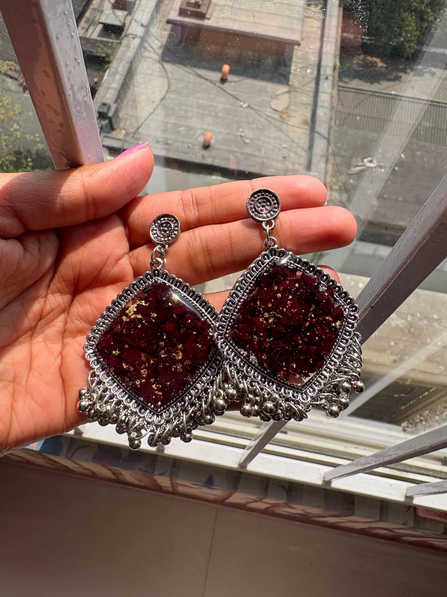Kite-shaped silver jhumkas packed with dark maroon rose petals and gold leaf in resin, with silver bead fringe