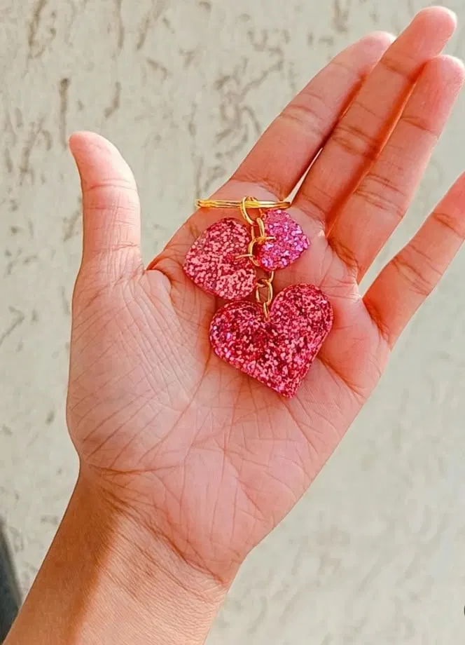 Three pink glitter resin hearts of different sizes on a gold keyring, held in an open palm