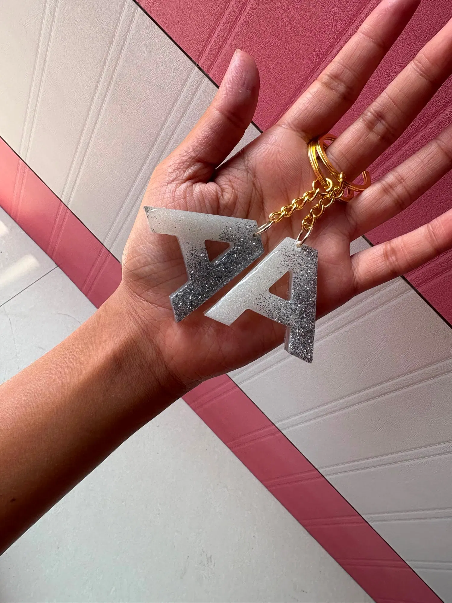 Two letter-A keychains in white and silver ombré glitter resin hanging from a gold chain, held in a hand