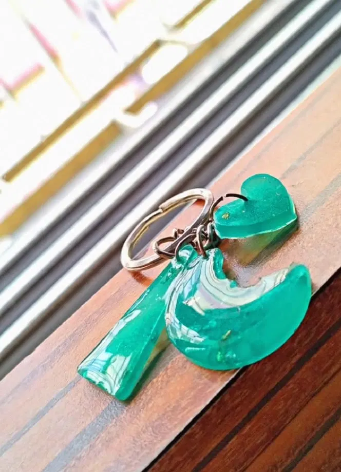 Three turquoise marbled resin charms (a heart, a wedge and a half-moon) on a silver keyring resting on a wooden ledge