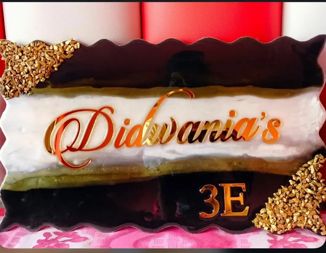 A dark brown and cream marbled resin name plate with a scalloped edge reading Didwania's 3E in rose-gold mirror script