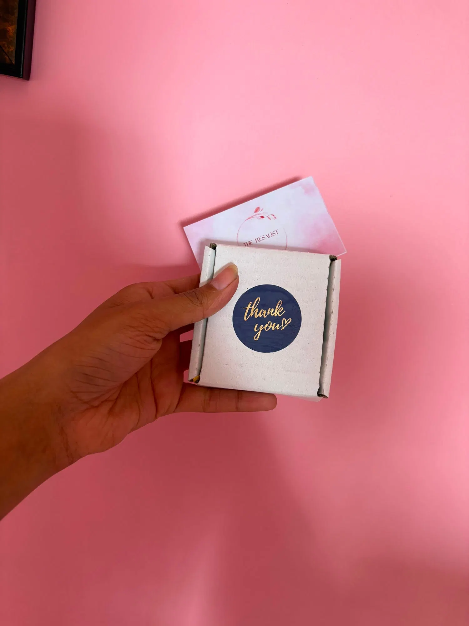 A white box with a navy and gold thank-you sticker, with the blush brand card tucked behind it