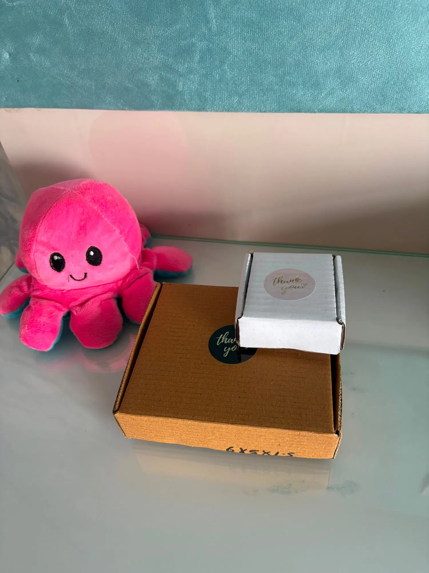 Two shipping boxes of different sizes side by side with thank-you stickers, next to a pink plush octopus