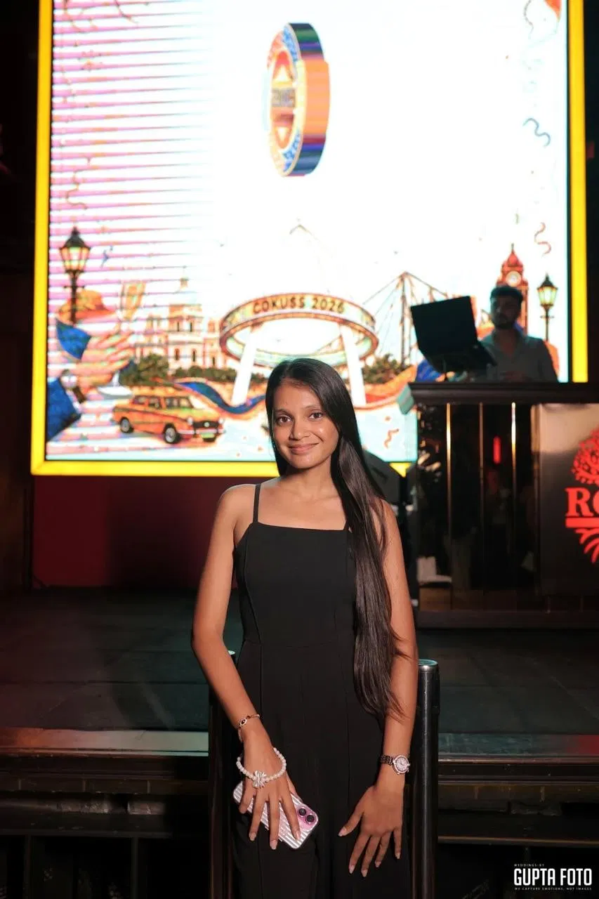 One of the sisters at an evening event, standing in front of an illuminated Kolkata-themed backdrop