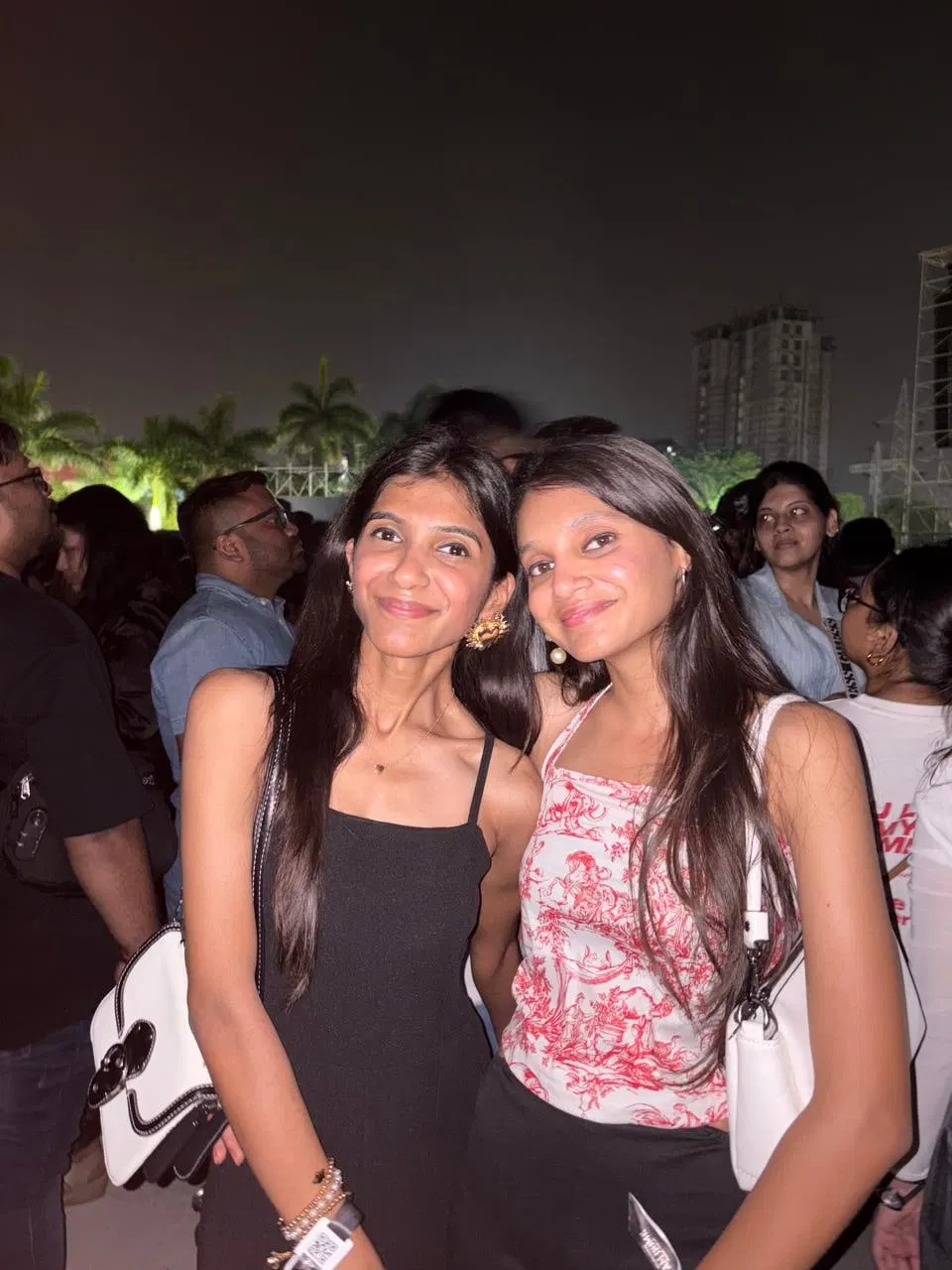 The two sisters together at an outdoor evening event, smiling at the camera