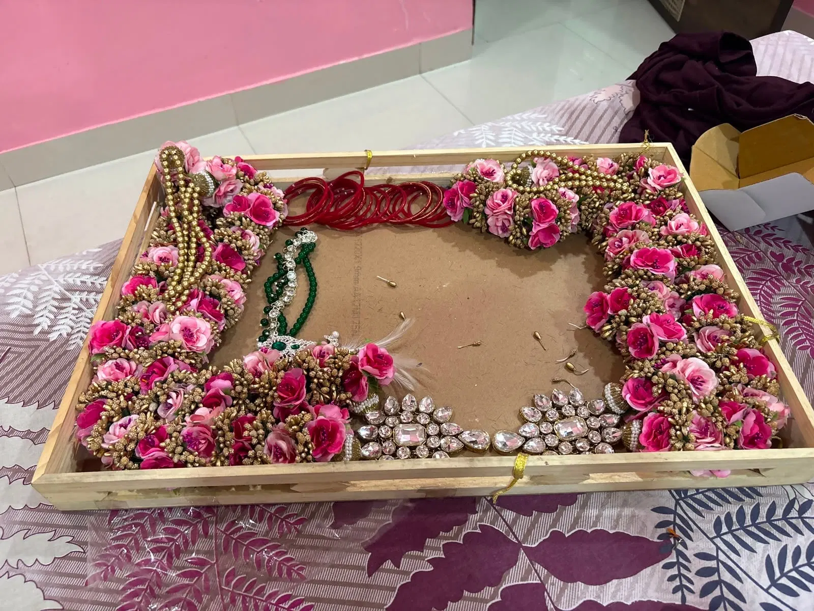 A varmala frame in progress: preserved roses arranged around three sides of the base with jewellery and bangles being positioned